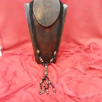 Bohemian style necklace featuring a Central wooden pendant paired with black beaded strands and accent beads