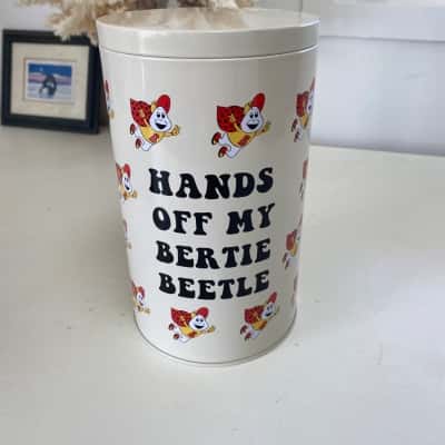 The White Cylindrical Tin Features Repeated Graphics Of iconic Australian Mascot Bertie Beetle Hands Off My Bertie Bettle