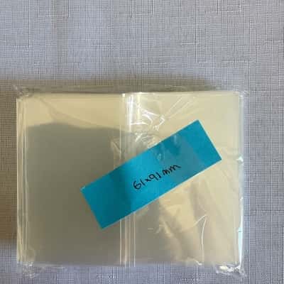 Pack of 100 protective sleeves for trading cards, with dimensions marked as 61x91mm,these are used to protect and preserve collectibles like trading cards or photo cards(B15)