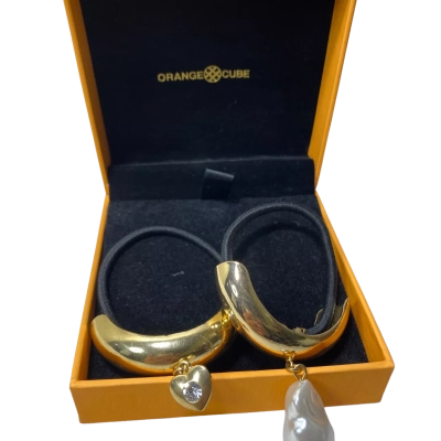  gold-tone Orange Cube hair ties featuring sculptural arches, one with a crystal heart charm and the other with a pearl drop charm. 