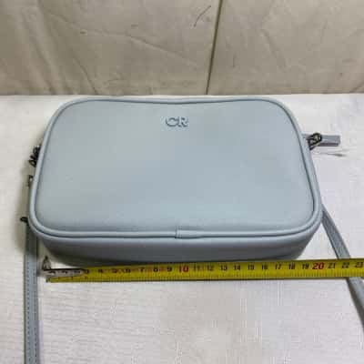 Country Road Tonal Camera Bag or a variation of their Branded/Contrast Camera Bag series. It is made with a textured Saffiano polyurethane finish and features the iconic powder-coated "CR" monogram hardware centered on the front. 21 x 14 x 4cm