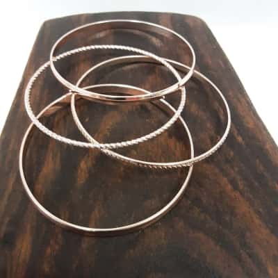 Delicate rose gold tone stacking bangles featuring charming mix of smooth and textured finishes