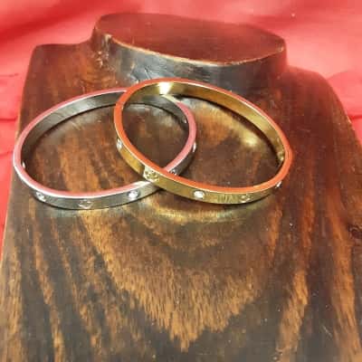 1 Gold Tone and 1 silver tone hinged bangles featuring engraved lucky Clover Motif and rhinestones